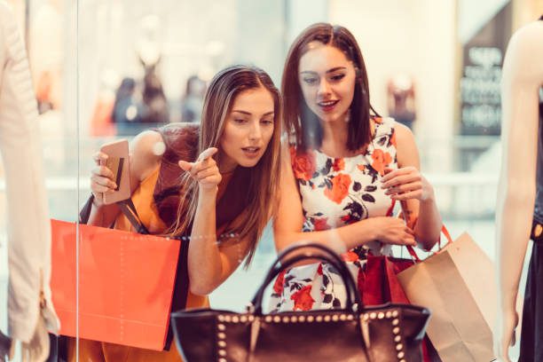 Happy women in the shopping mall looking at the shop window - Bidaya Global