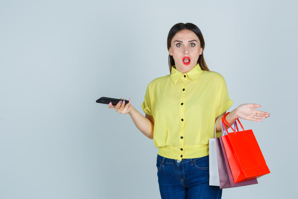 young female in blouse jeans holding pockets while keeping mobile phone and looking puzzled front view - Bidaya Global